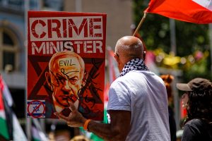 man holding a sign "Crime Minister" with an image Netanyahu.