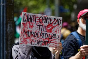 Person holding a sign that says "what crime did the murdered child commit".