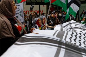 People chanting "ceasefire now" holding a giant keffiyeh