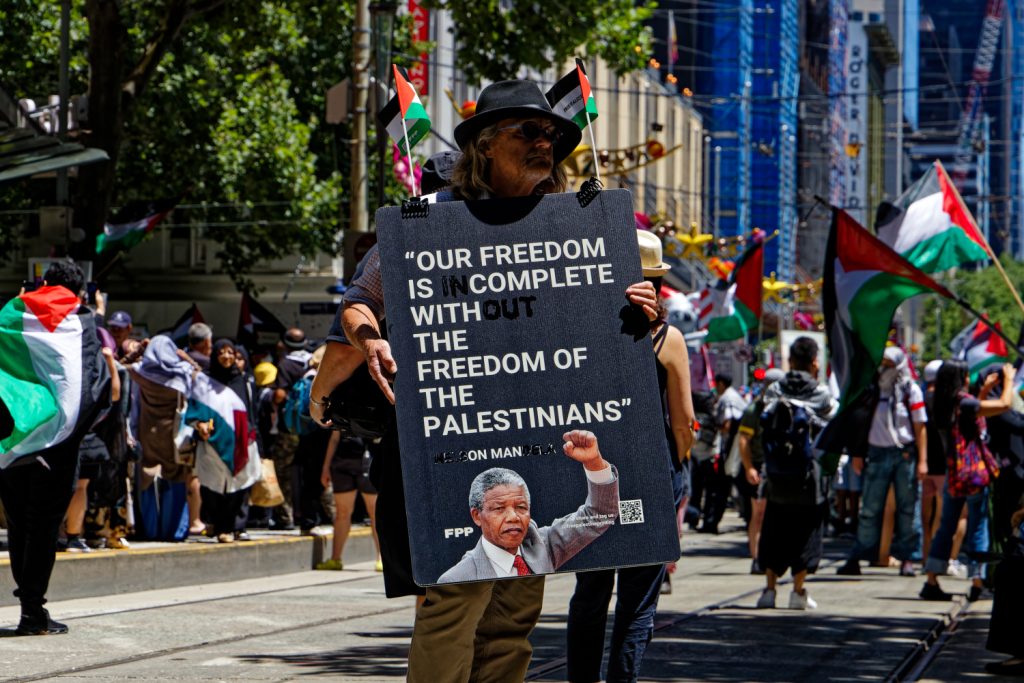 Man holding a banner saying "Our freedom is complete with the freedom of the Palestinians" (a cheeky misquote), with a photo of Nelson Mandela - 17 December. Photo: Wayne Jansson